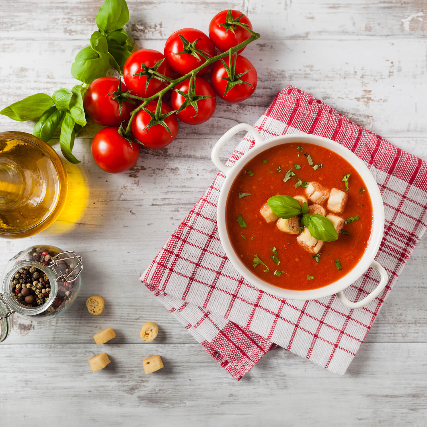 Schale mit cremiger Tomatensuppe, garniert mit frischem Basilikum, serviert auf kariertem Tuch